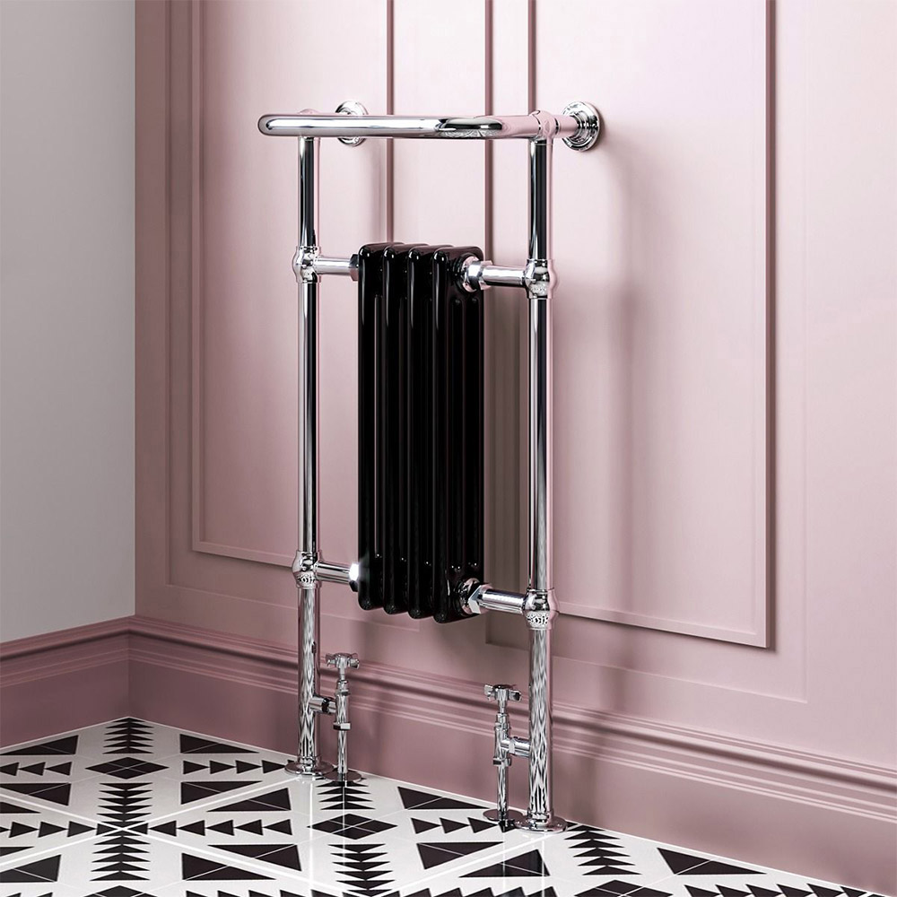 Small black radiator, close up with tap like valves against a pink wall with black and white geometric flooring
