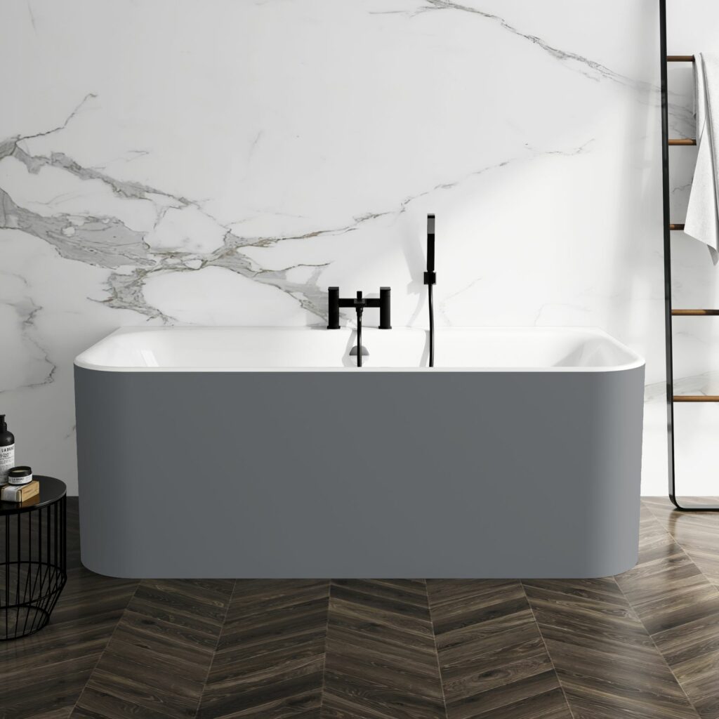 Slate grey acrylic back to wall bath in a marble tiled bathroom with dark wood effect chevron flooring